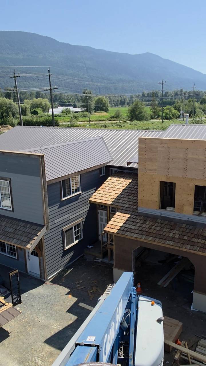 One wing in grey siding, the tower still in plywood, metal roofs on