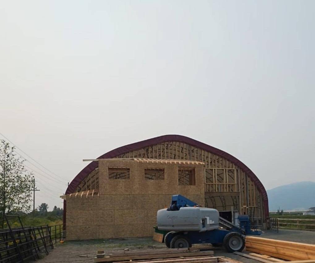 Arena end wall in OSB under the red arch, lift and lumber in the yard