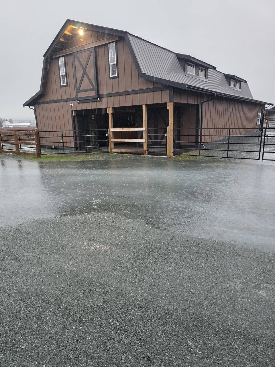Finished brown gambrel barn with a metal roof and pipe-panel fence