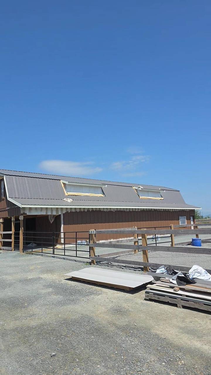 Long side of a brown barn with a metal roof and two dormers