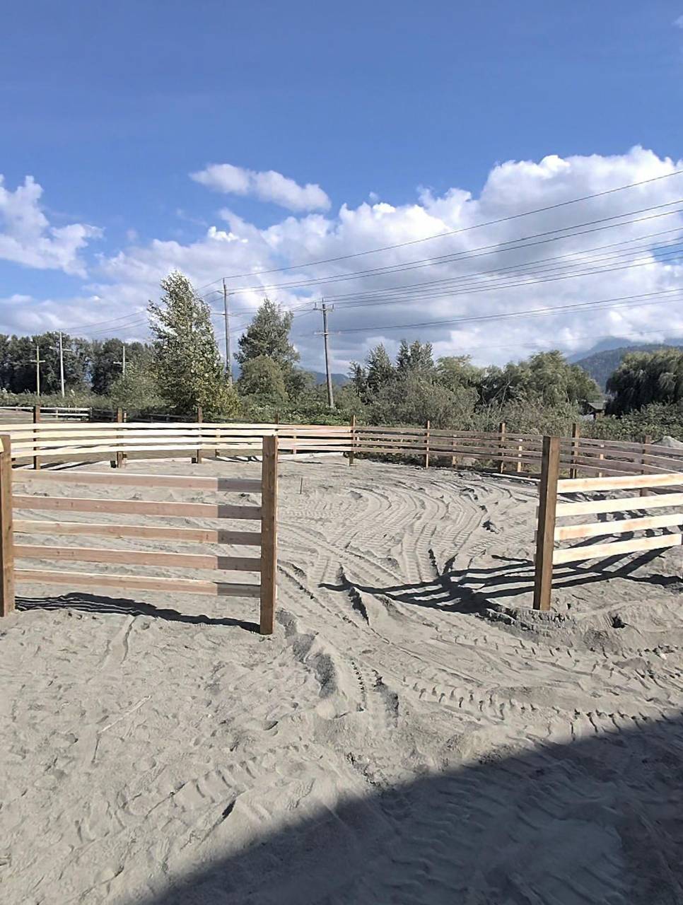 Four-rail wood fence opening onto a sand riding pen