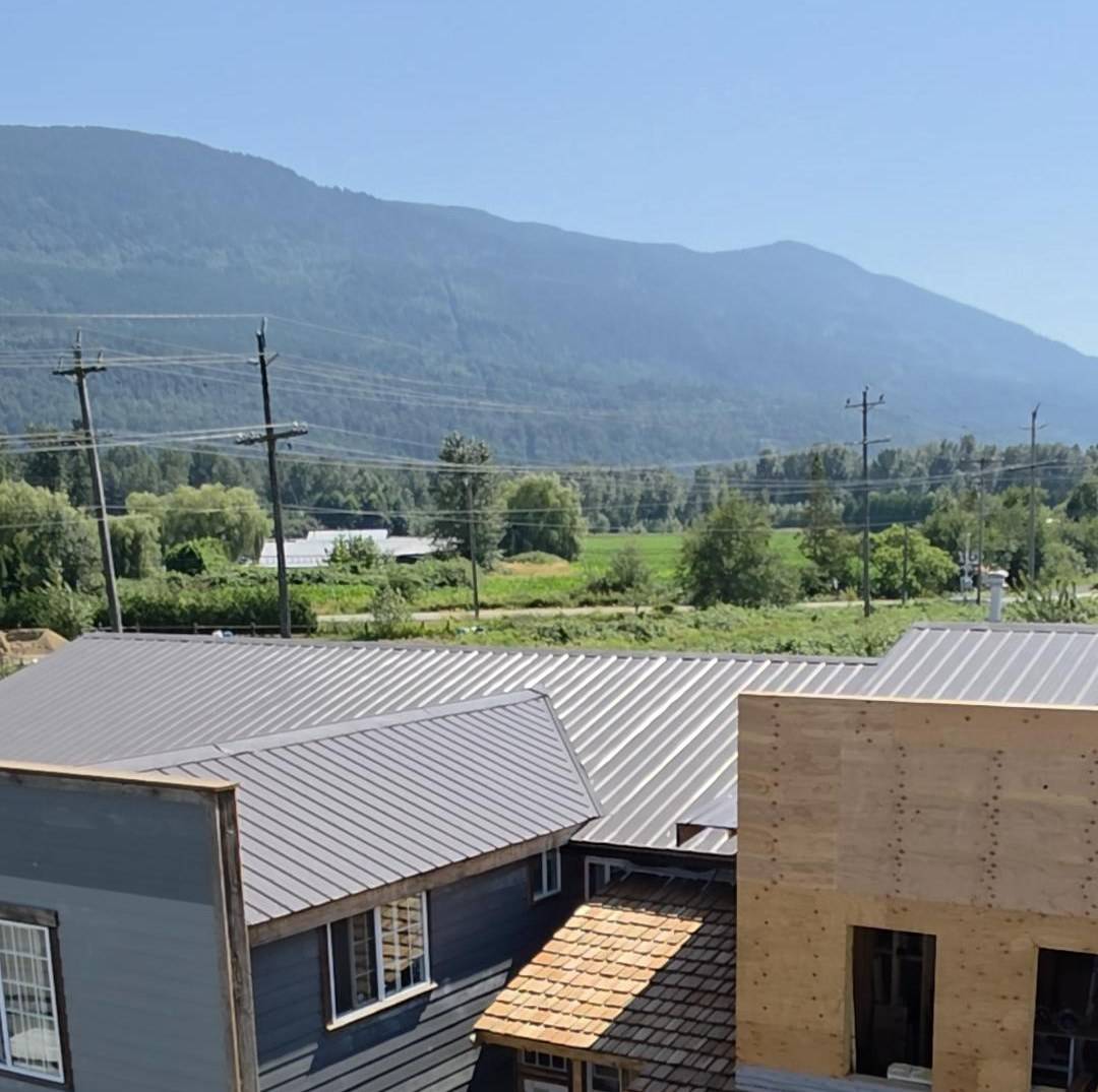 Grey siding and cedar-shake roofs on a house, the upper storey still in plywood