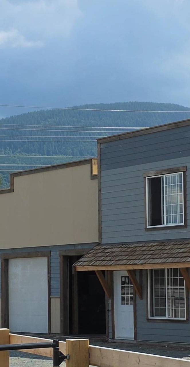 Grey and beige siding with a cedar-shake porch, seen past a wood fence
