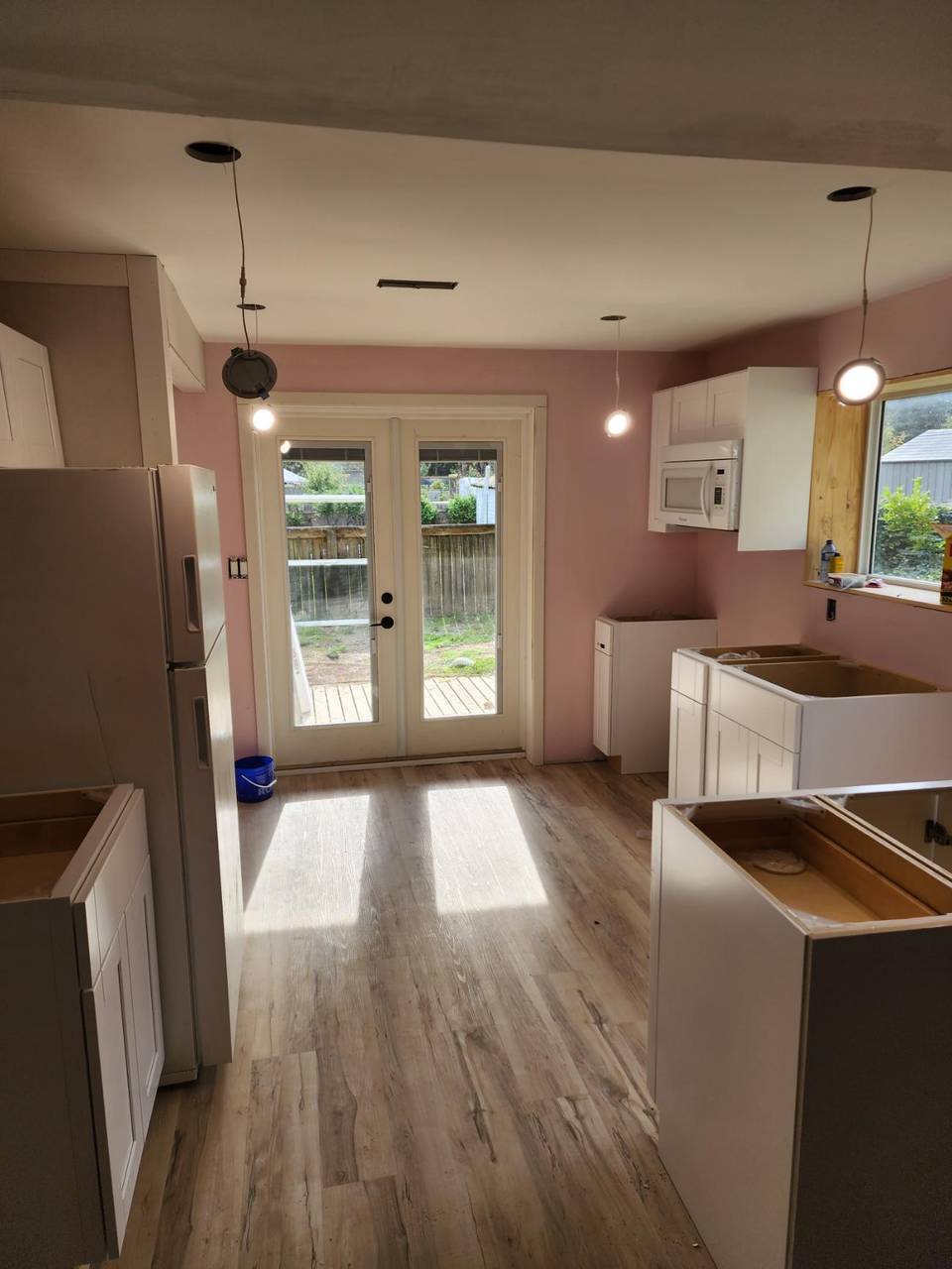Kitchen mid-build with cabinets set, flooring down, and doors to the yard