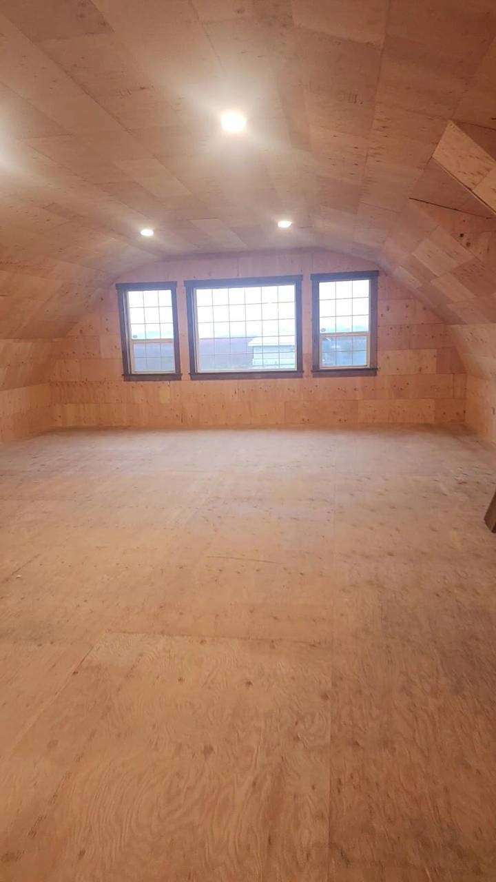Finished plywood loft inside a gambrel barn, three windows on the end wall