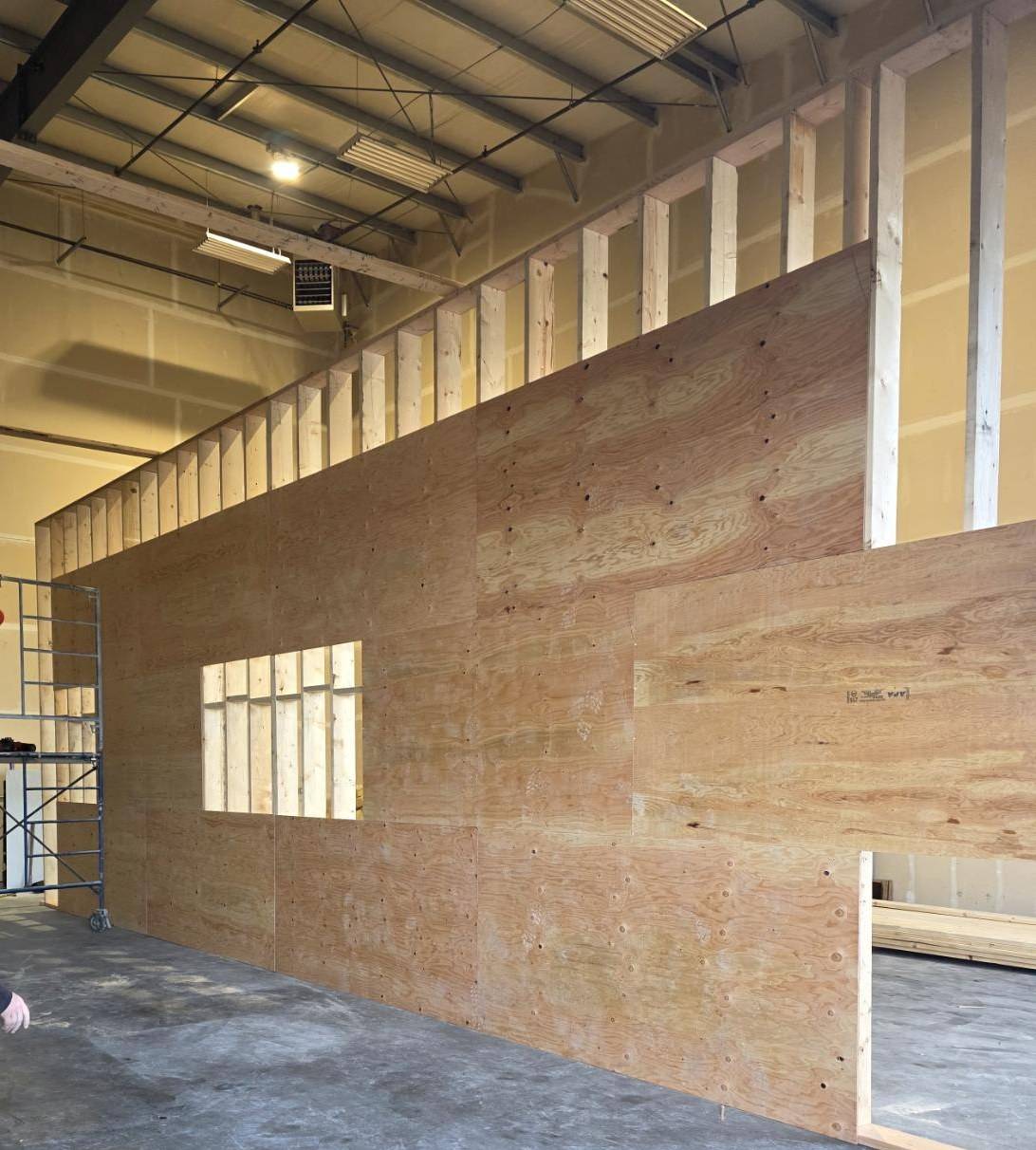 Tall shop wall sheathed in plywood, openings cut for a window and a door